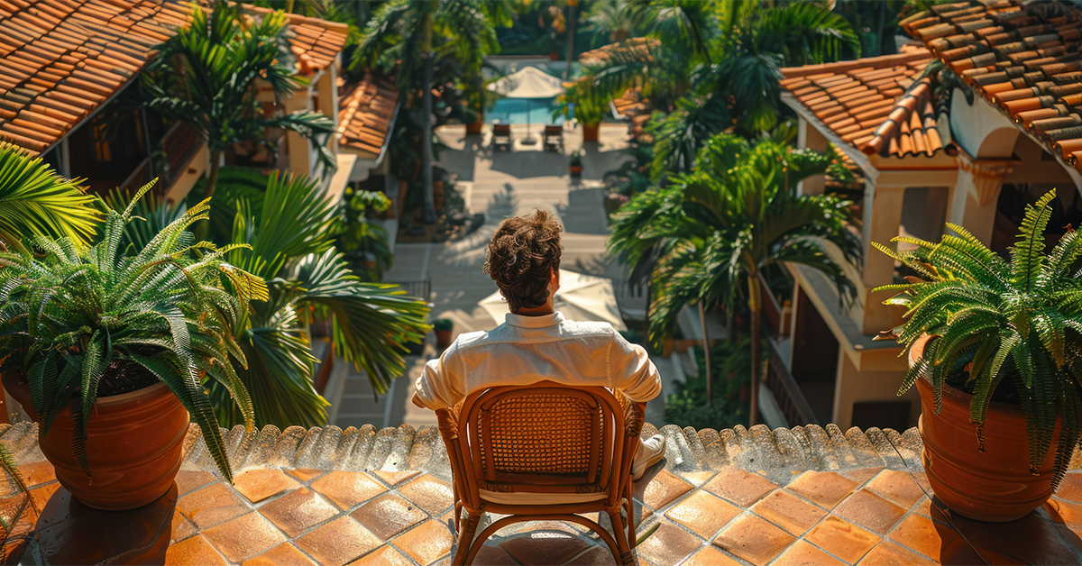 Tourist sitting on a terrace overlooking a tropical resort with palm trees and villas, illustrating tourism-driven real estate growth.