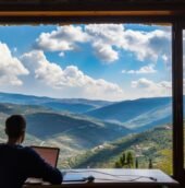 A person working remotely on a laptop while enjoying a scenic mountain view, representing Workation destinations in India.