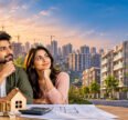Affordable homes in India featuring a young couple reviewing property plans, with modern residential apartments and high-rise buildings in the background.