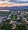 Aerial view of Chandigarh Tricity featuring urban neighborhoods, green spaces, a stadium, lakes, and mountain ranges at sunset.