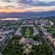 Aerial view of Chandigarh Tricity featuring urban neighborhoods, green spaces, a stadium, lakes, and mountain ranges at sunset.