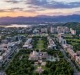 Aerial view of Chandigarh Tricity featuring urban neighborhoods, green spaces, a stadium, lakes, and mountain ranges at sunset.