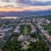 Aerial view of Chandigarh Tricity featuring urban neighborhoods, green spaces, a stadium, lakes, and mountain ranges at sunset.