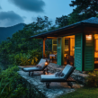 Cozy Coorg homestay surrounded by lush greenery, with mountain views, outdoor lounge chairs, and warm interior lighting.
