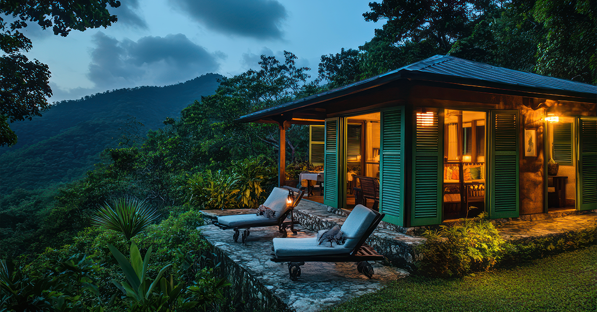Cozy Coorg homestay surrounded by lush greenery, with mountain views, outdoor lounge chairs, and warm interior lighting.