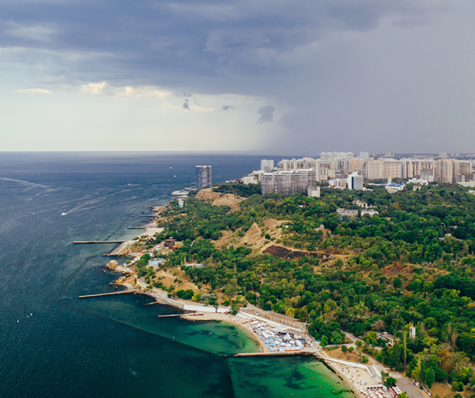 Aerial view of a scenic coastal city with the sea, green landscape, beaches, and modern buildings, highlighting Goa real estate investment opportunities.