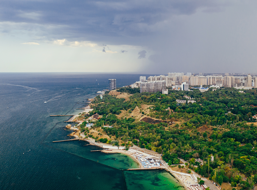 Aerial view of a scenic coastal city with the sea, green landscape, beaches, and modern buildings, highlighting Goa real estate investment opportunities.