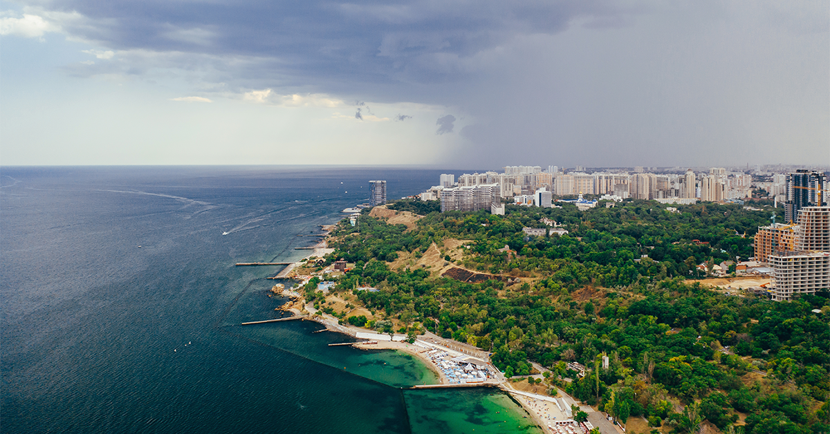 Aerial view of a scenic coastal city with the sea, green landscape, beaches, and modern buildings, highlighting Goa real estate investment opportunities.
