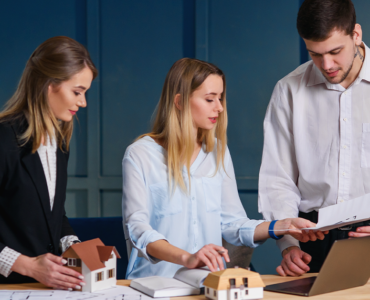 Professionals discussing real estate investment as part of long-term wealth planning with property models and financial documents