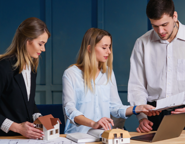 Professionals discussing real estate investment as part of long-term wealth planning with property models and financial documents