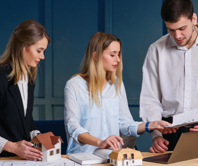 Professionals discussing real estate investment as part of long-term wealth planning with property models and financial documents