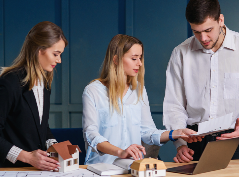 Professionals discussing real estate investment as part of long-term wealth planning with property models and financial documents