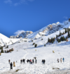 Snow-covered mountain slopes with skiers and tourists enjoying a winter landscape under a clear blue sky.