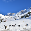 Snow-covered mountain slopes with skiers and tourists enjoying a winter landscape under a clear blue sky.