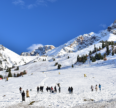 Snow-covered mountain slopes with skiers and tourists enjoying a winter landscape under a clear blue sky.
