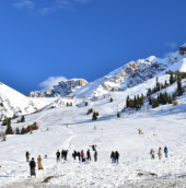 Snow-covered mountain slopes with skiers and tourists enjoying a winter landscape under a clear blue sky.