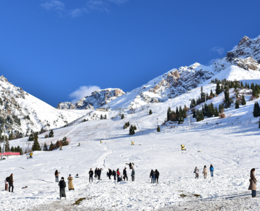Snow-covered mountain slopes with skiers and tourists enjoying a winter landscape under a clear blue sky.