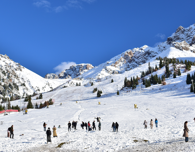 Snow-covered mountain slopes with skiers and tourists enjoying a winter landscape under a clear blue sky.