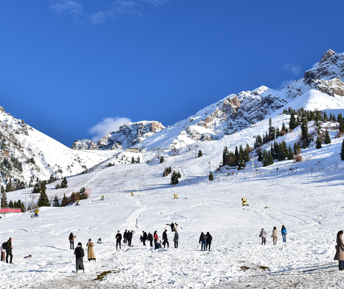 Snow-covered mountain slopes with skiers and tourists enjoying a winter landscape under a clear blue sky.