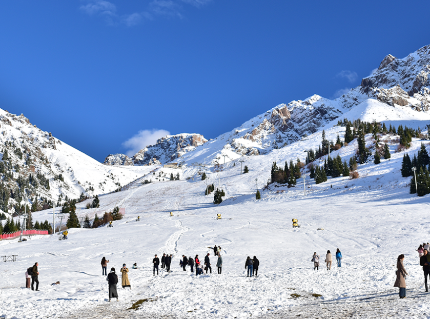 Snow-covered mountain slopes with skiers and tourists enjoying a winter landscape under a clear blue sky.