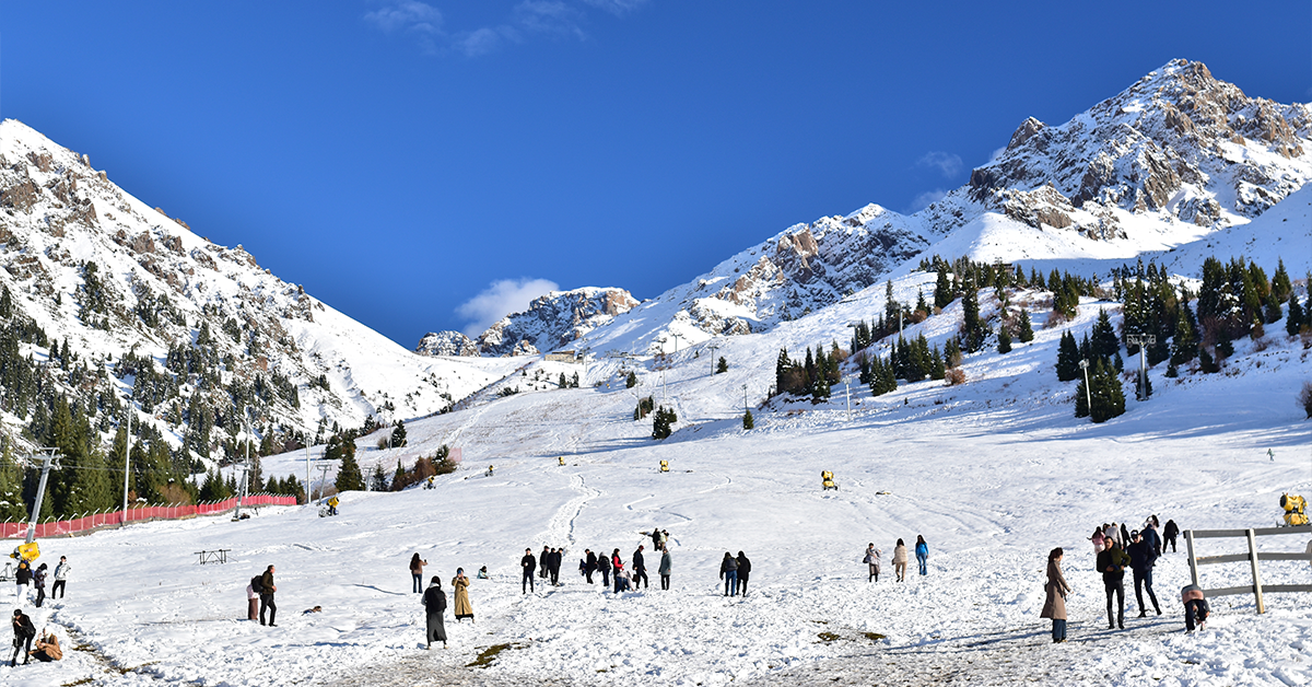Snow-covered mountain slopes with skiers and tourists enjoying a winter landscape under a clear blue sky.