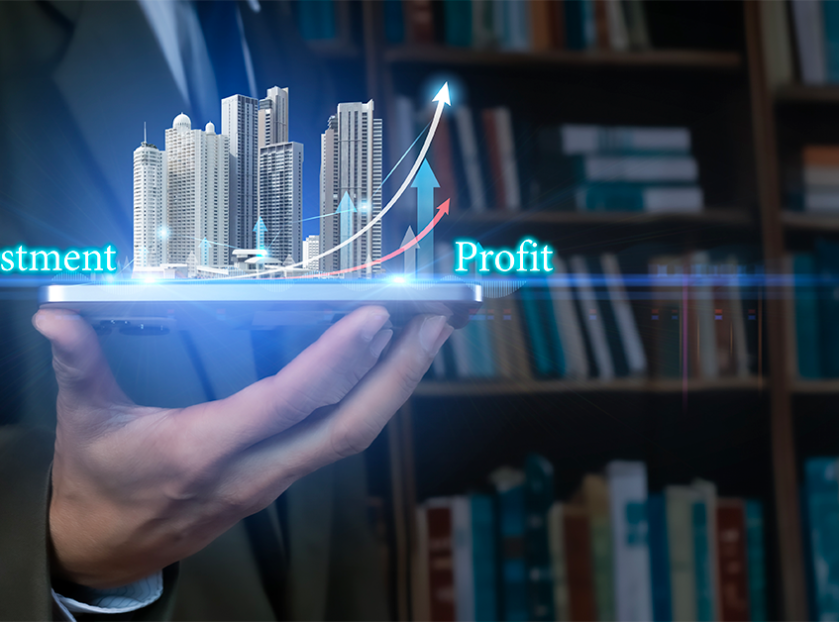Hand holding a tablet displaying a digital real estate investment concept, with high-rise buildings, rising arrows, and the words “Investment” and “Profit.”