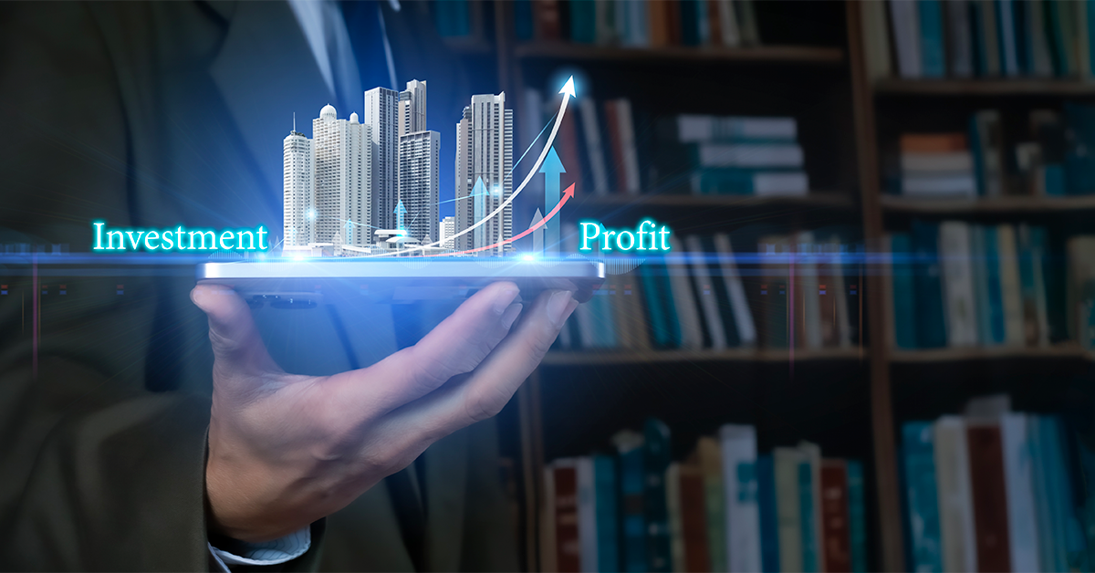 Hand holding a tablet displaying a digital real estate investment concept, with high-rise buildings, rising arrows, and the words “Investment” and “Profit.”
