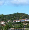 Scenic South Indian hill landscape with lush green hills, white houses with red-tiled roofs, and a bright blue sky.