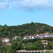 Scenic South Indian hill landscape with lush green hills, white houses with red-tiled roofs, and a bright blue sky.