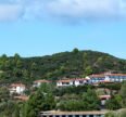 Scenic South Indian hill landscape with lush green hills, white houses with red-tiled roofs, and a bright blue sky.