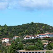 Scenic South Indian hill landscape with lush green hills, white houses with red-tiled roofs, and a bright blue sky.