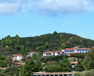 Scenic South Indian hill landscape with lush green hills, white houses with red-tiled roofs, and a bright blue sky.