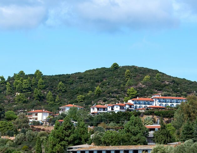 Scenic South Indian hill landscape with lush green hills, white houses with red-tiled roofs, and a bright blue sky.