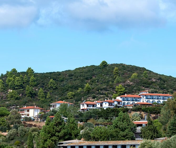 Scenic South Indian hill landscape with lush green hills, white houses with red-tiled roofs, and a bright blue sky.