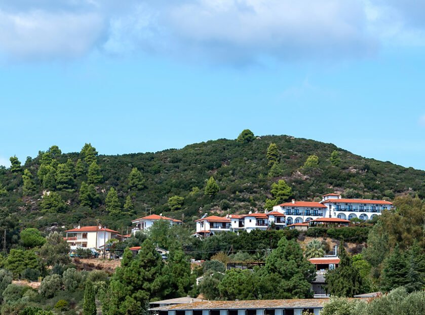 Scenic South Indian hill landscape with lush green hills, white houses with red-tiled roofs, and a bright blue sky.