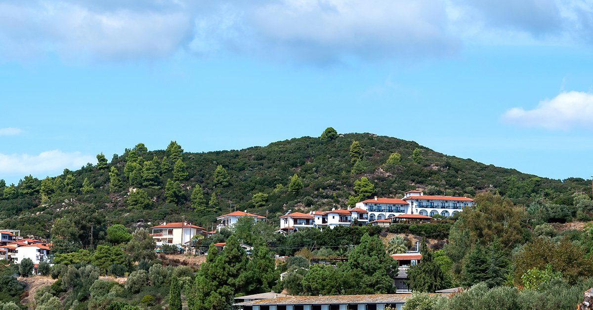 Scenic South Indian hill landscape with lush green hills, white houses with red-tiled roofs, and a bright blue sky.