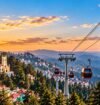 Shimla ropeway with red cable cars overlooking the city, pine forests, and Himalayan mountains at sunset.