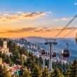 Shimla ropeway with red cable cars overlooking the city, pine forests, and Himalayan mountains at sunset.