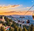 Shimla ropeway with red cable cars overlooking the city, pine forests, and Himalayan mountains at sunset.