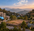 Kasauli apartments surrounded by lush green hills, featuring modern architecture and contrasting arrows illustrating real estate price trends at sunset.