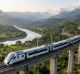 Vande Bharat train traveling on an elevated railway bridge through lush green mountains, overlooking a winding river and scenic valley.