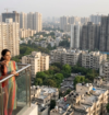 Homebuyers reviewing residential property prices in India with a real estate agent overlooking a city skyline of high-rise apartments under construction.
