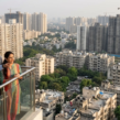 Homebuyers reviewing residential property prices in India with a real estate agent overlooking a city skyline of high-rise apartments under construction.
