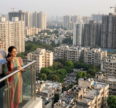 Homebuyers reviewing residential property prices in India with a real estate agent overlooking a city skyline of high-rise apartments under construction.