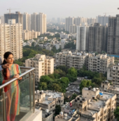 Homebuyers reviewing residential property prices in India with a real estate agent overlooking a city skyline of high-rise apartments under construction.